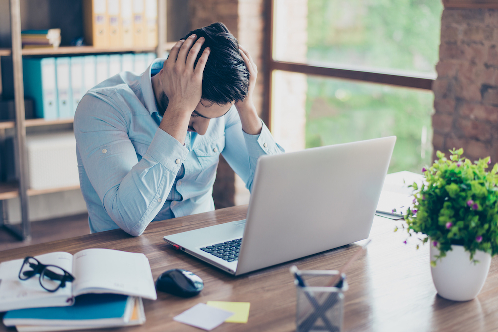 Frustrated man at laptop with head in hands