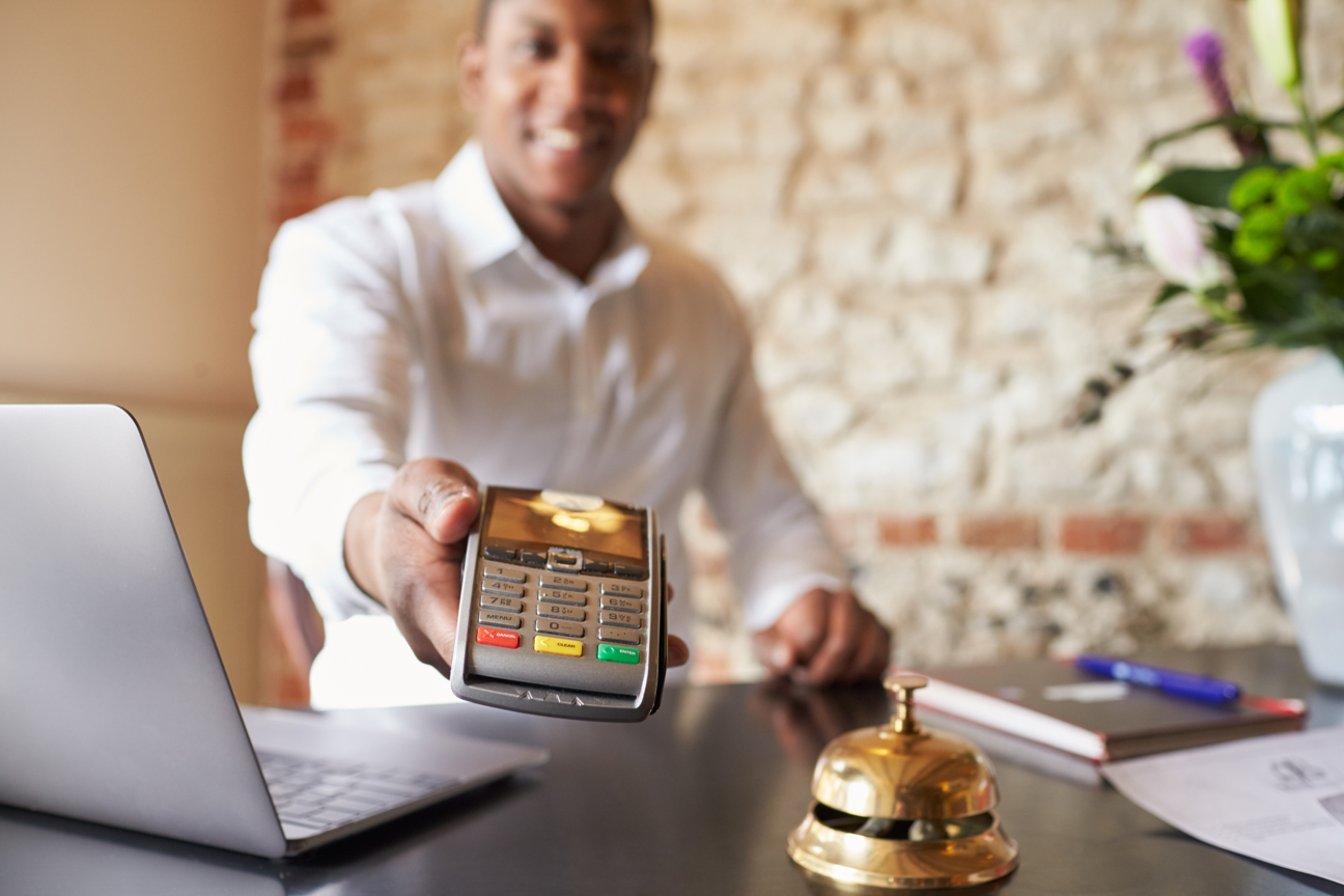 Concierge at hotel reception holds credit card reader to camera