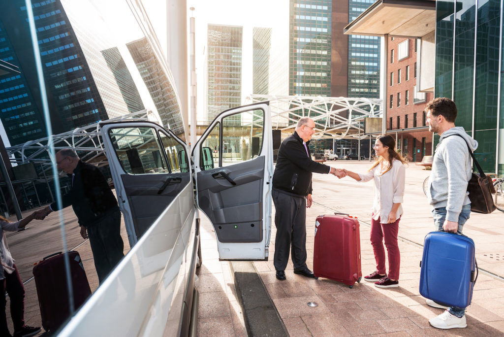 Driver of a airport shuttle minivan, greeting his passengers with their luggage