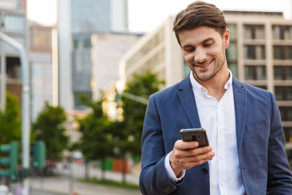 Handsome smiling young businessman smartly dressed standing outdoors at the city street, holding mob