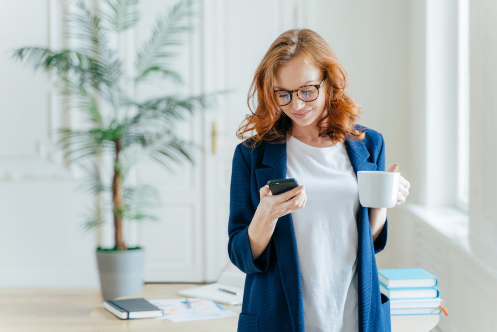 Successful Female Ceo Reads Notification On Modern Cell Phone, Has Coffee Break, Dressed In Formal C