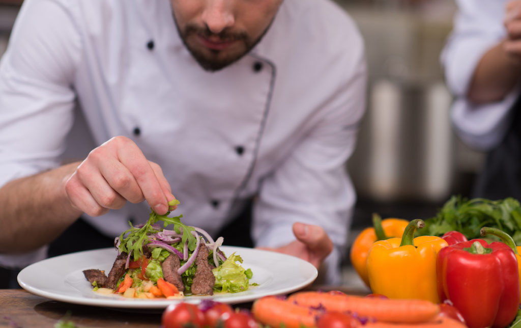 chef decorating garnishing prepared meal dish on the plate in restaurant