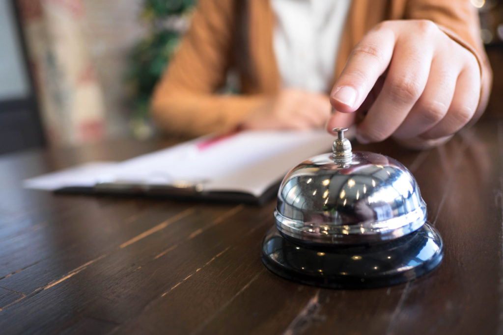 Women call hotel reception with finger push a bell in lobby hotel.