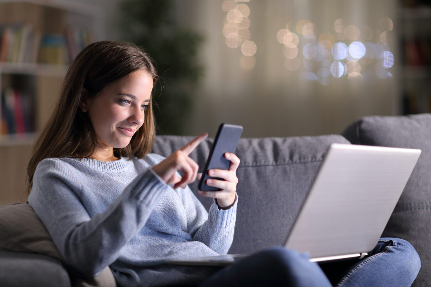 Woman Using Social Media on Phone and Laptop at Home