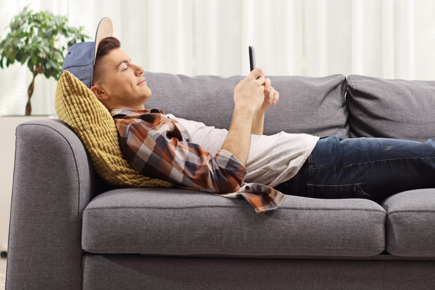 Young guy lying on a sofa and looking at a mobile phone at home
