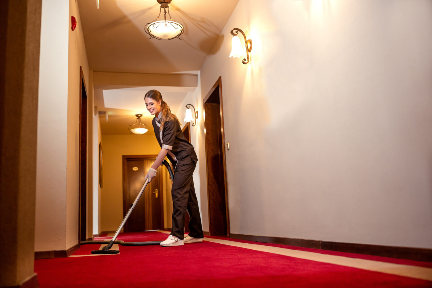 Housekeeping staff vacuuming an empty hallway
