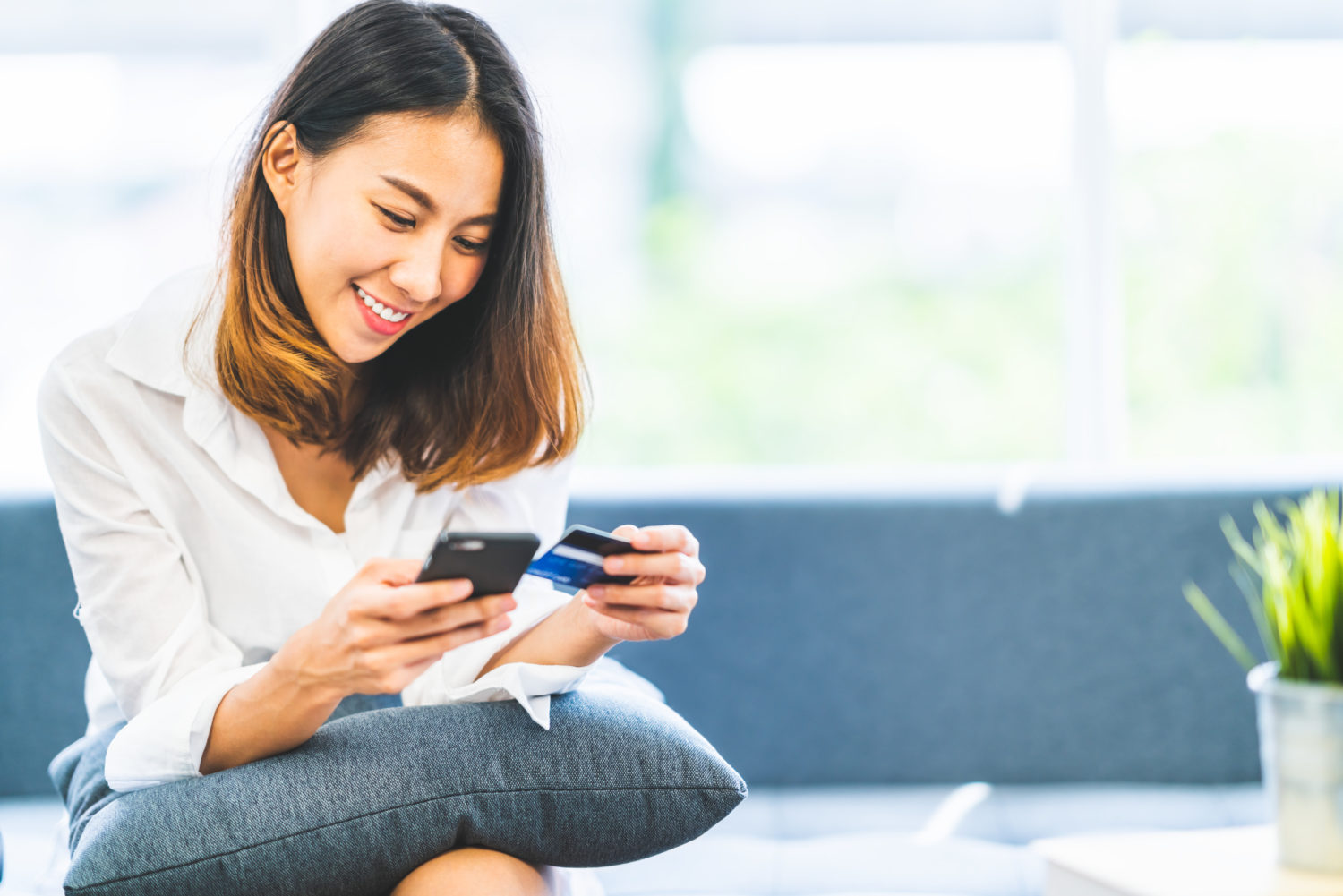 A young woman sitting on a couch using her credit card to book a hotel from her phone