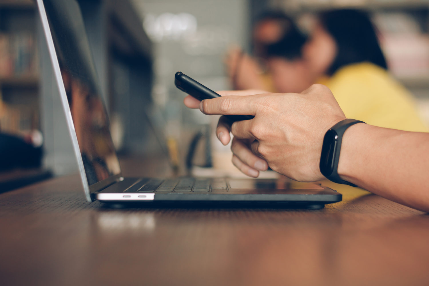 Close-up of hands holding a phone in front of a laptop