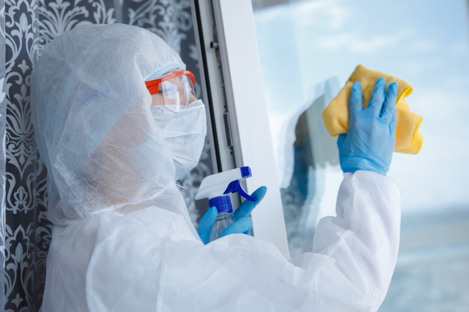 Woman wearing protective biohazard gear cleaning a window