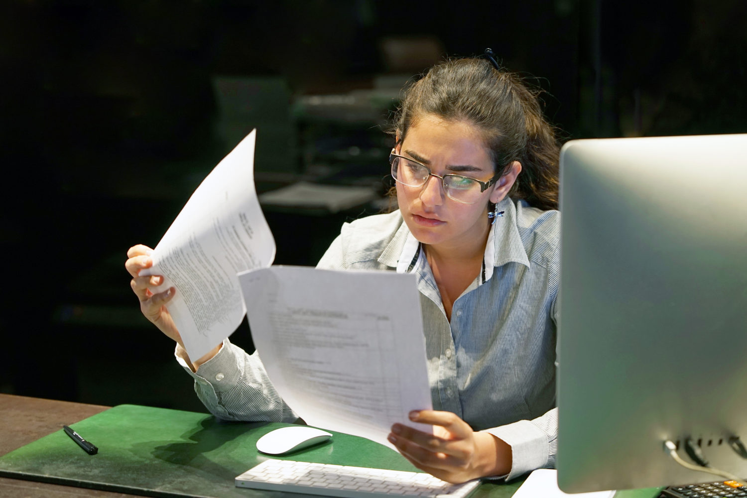 woman at computer reading paper with concentrated look on her face