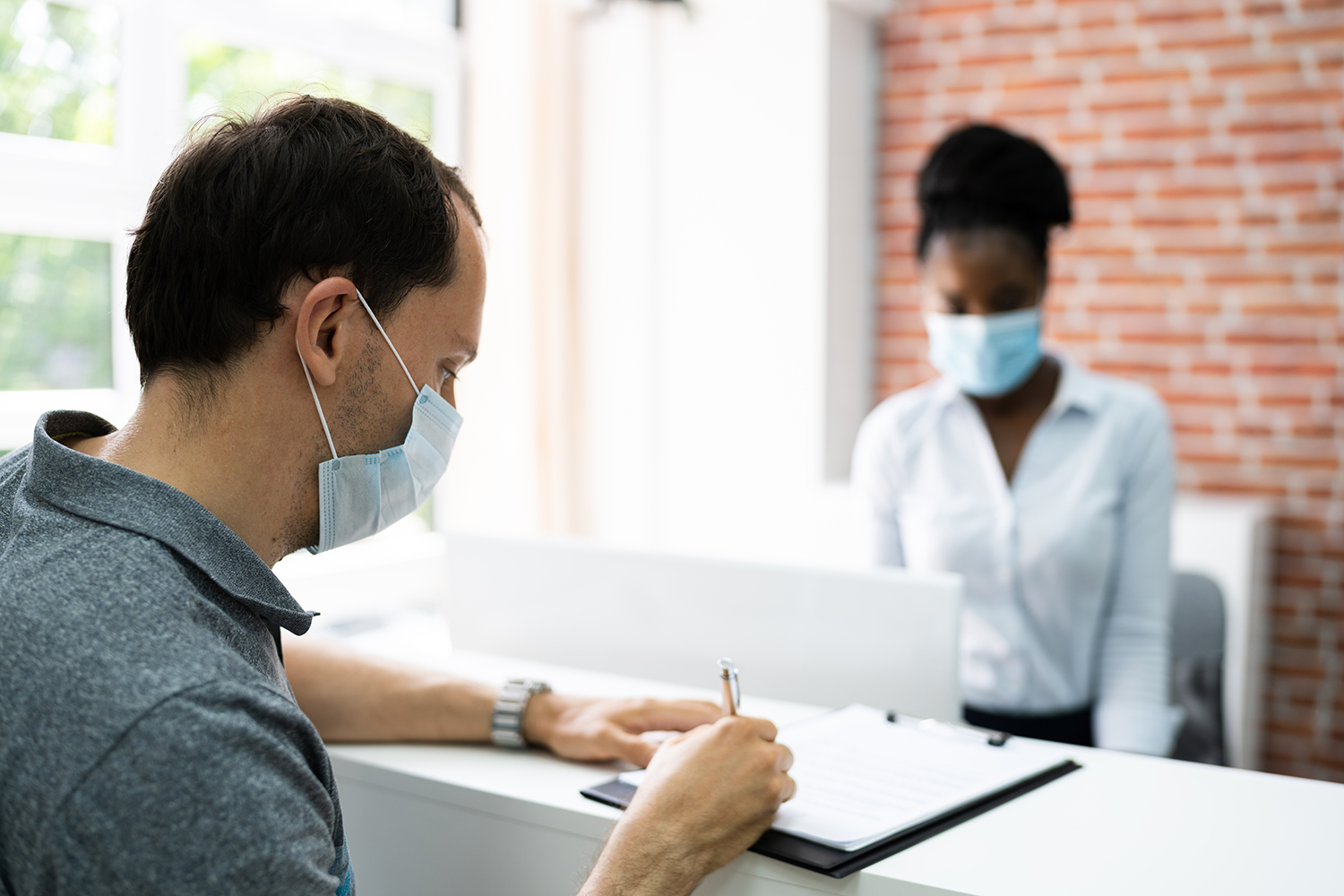 man checking in to hotel wearing face mask and receptionist is also wearing a face mask