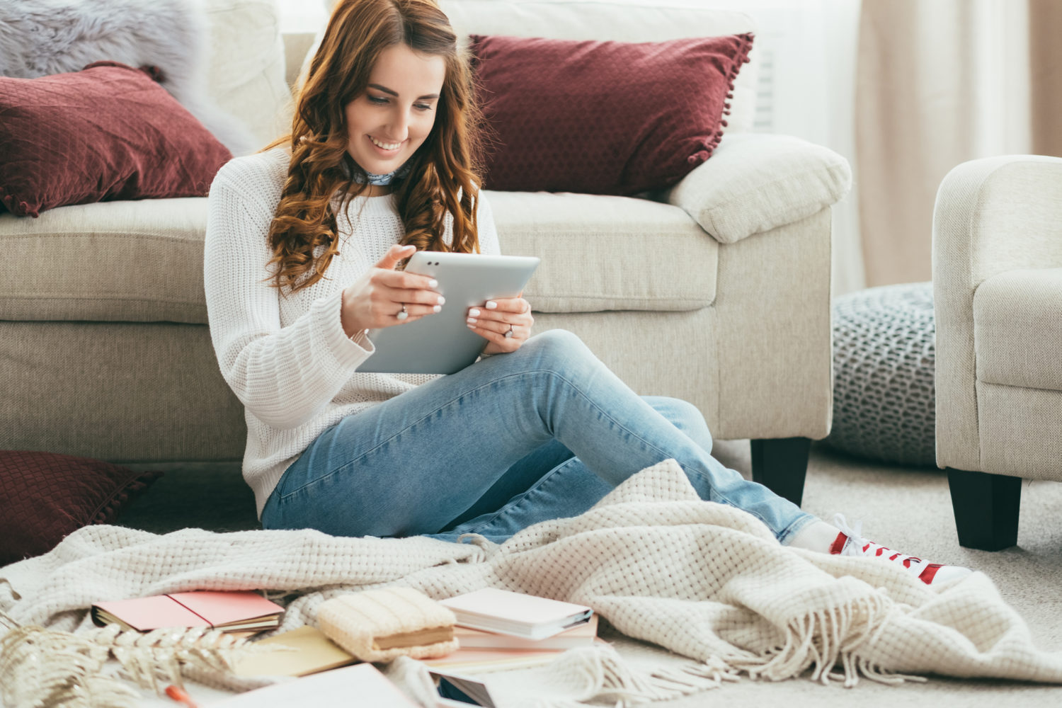 young woman sits on a blanket with books around her as she shops on her tablet