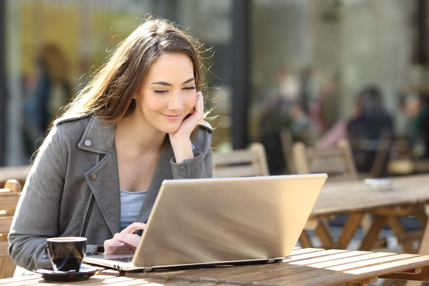 woman smiling at her laptop while sitting outdoors