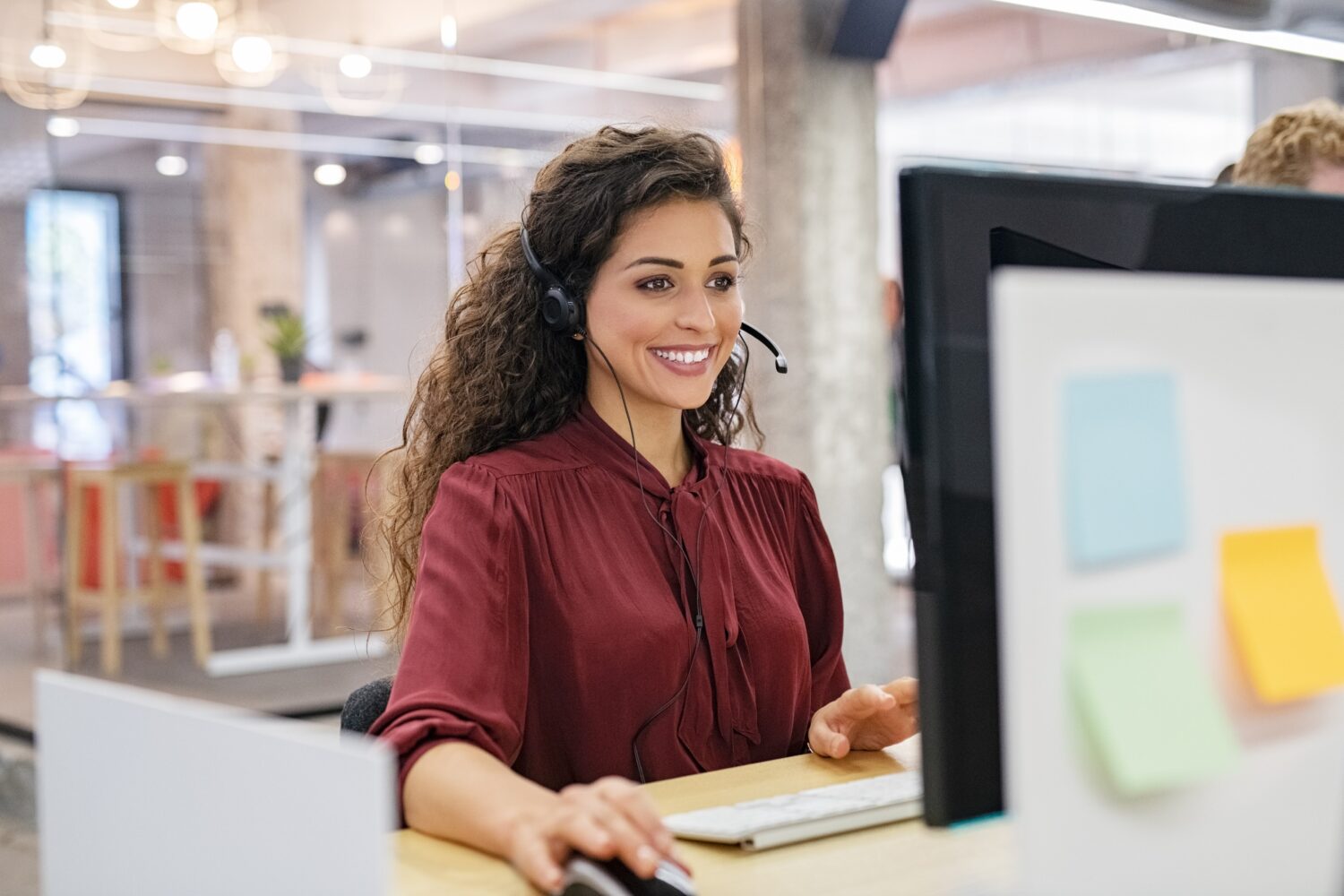 woman facing her computer wearing a headset and smiling