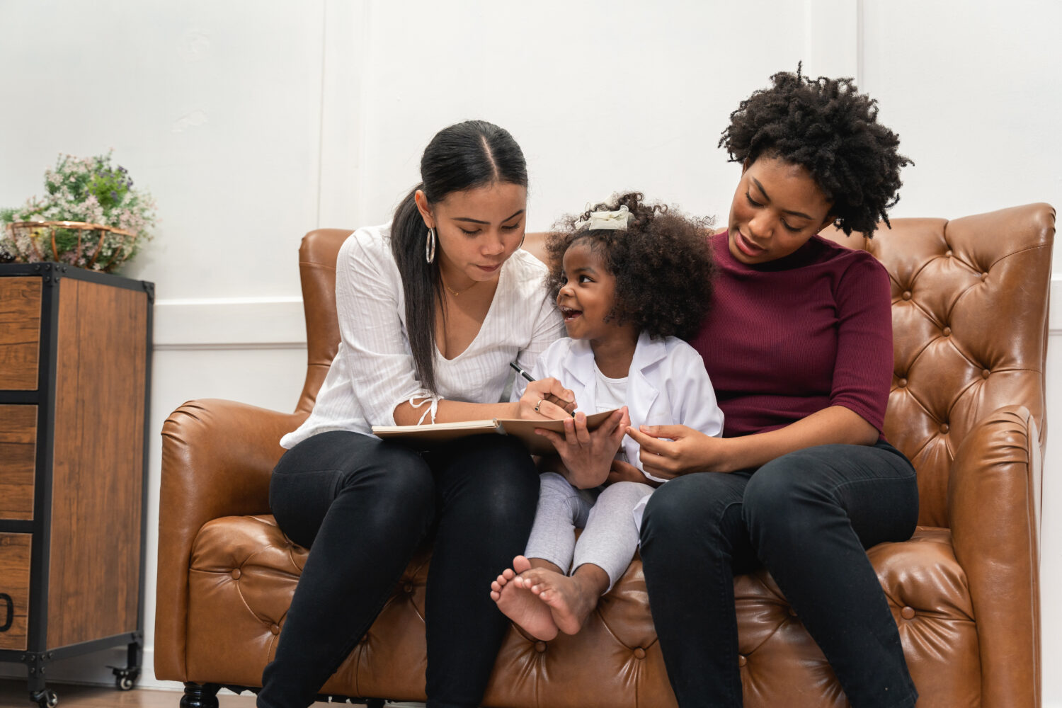 black lesbian mothers write in a notebook with their daughter between them