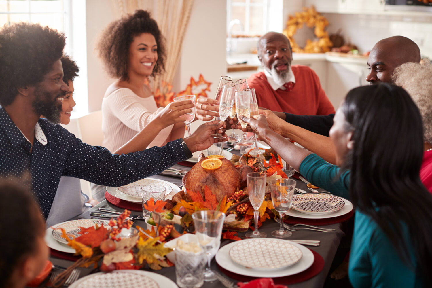 a large black family sits around a table and cheers glasses together