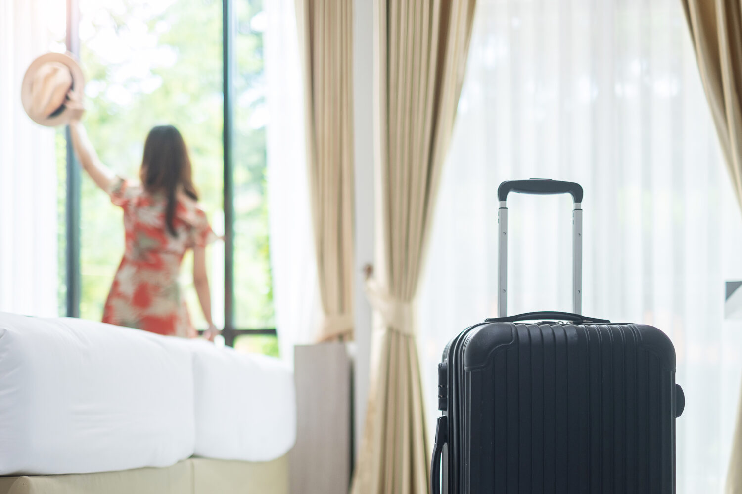 rolling suitcase in the foreground and a woman holding out a hat in the background