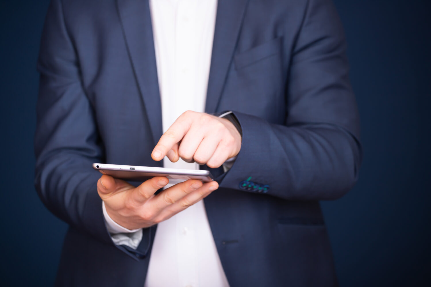 the shoulders and torso of a man in a suit using a tablet