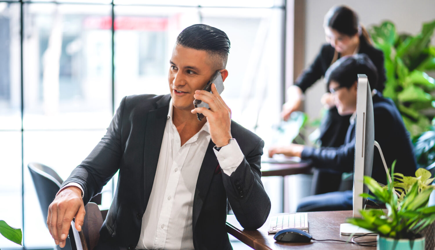 businessman facing sideways at his desk and speaking on a cell phone