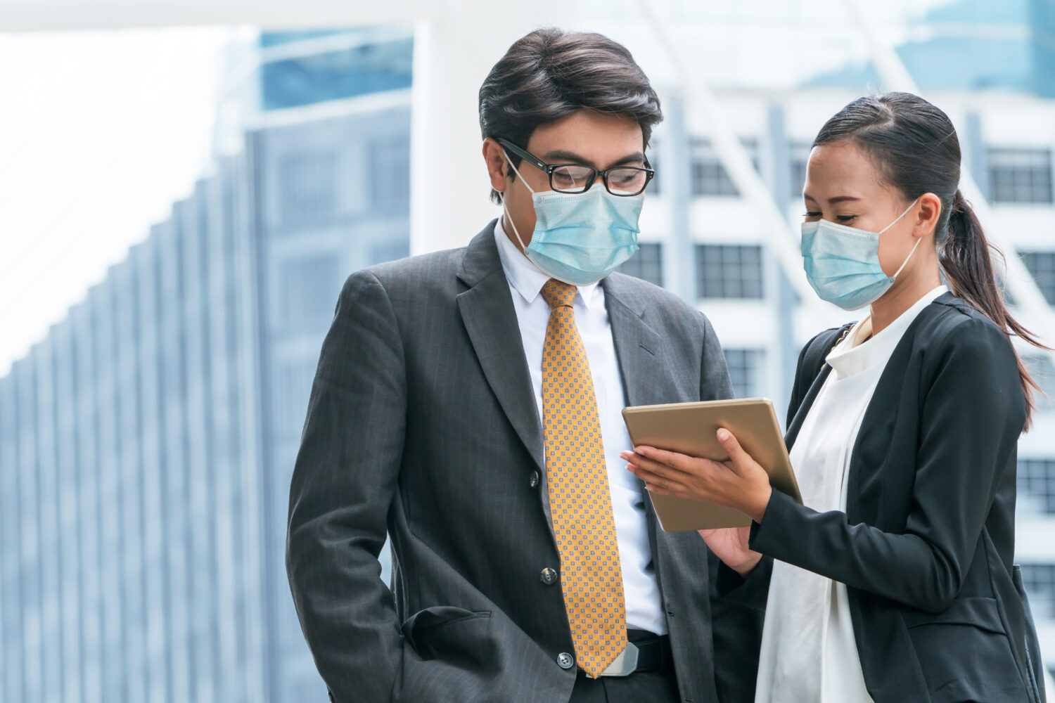 businessman and businesswoman wearing surgical masks discussing over a tablet