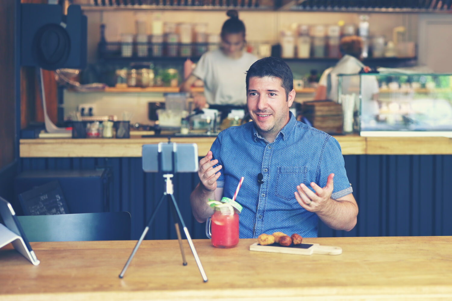 man with blue shirt recording himself using a tripod and camera at a restaurant