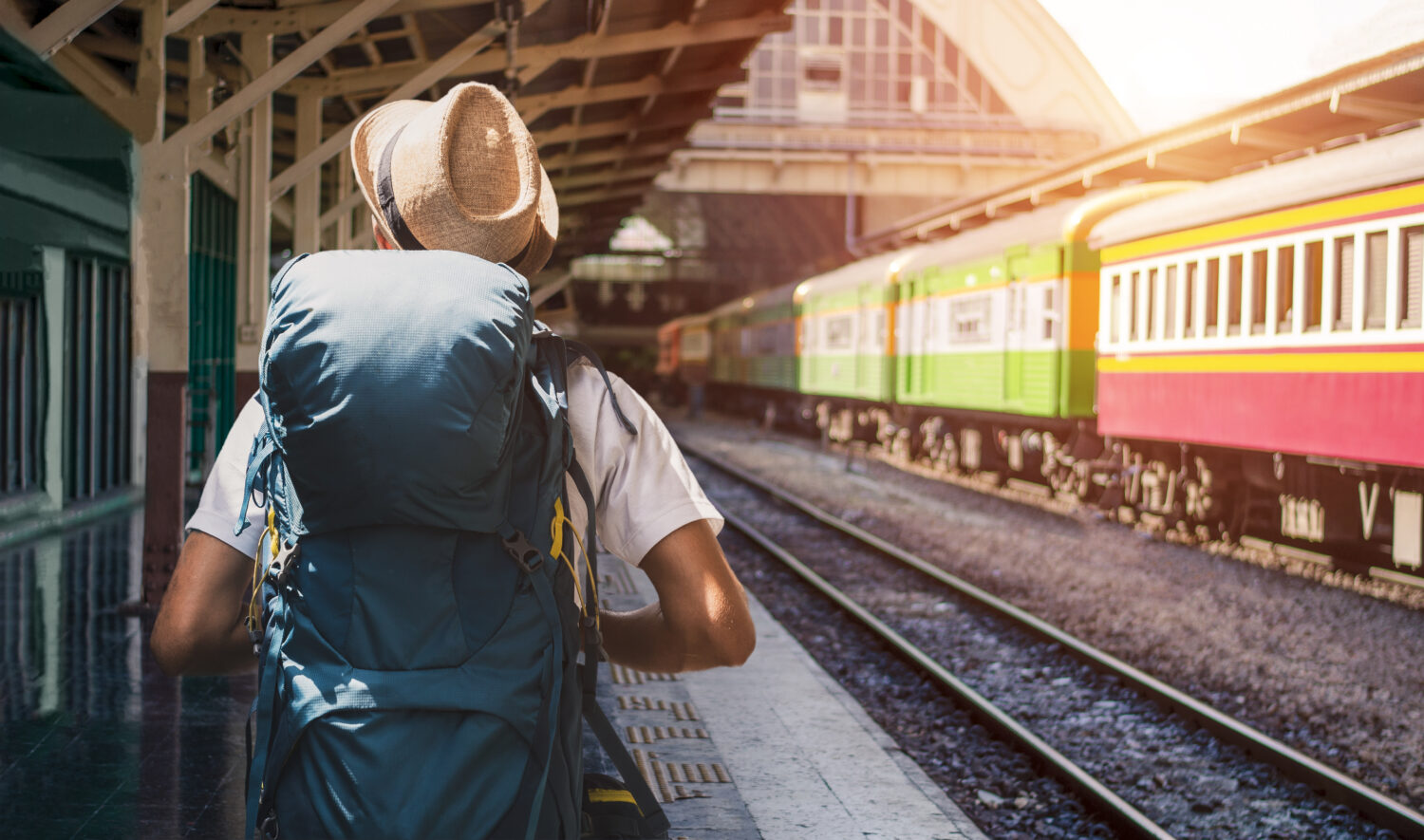 back of a man wearing a backpack and hat waiting for a train