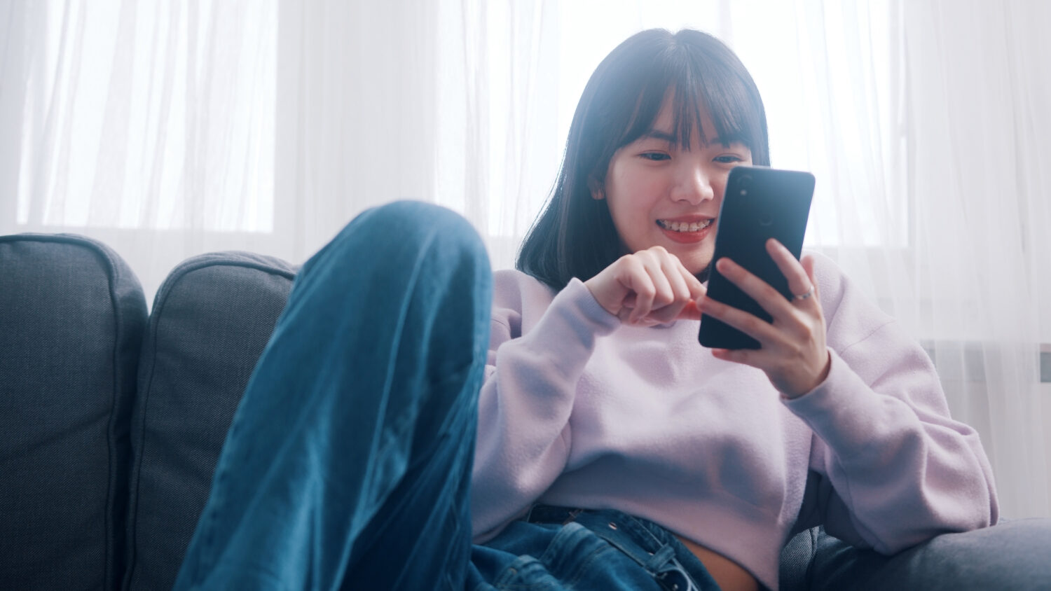 young asian woman sitting on a couch smiling at her phone