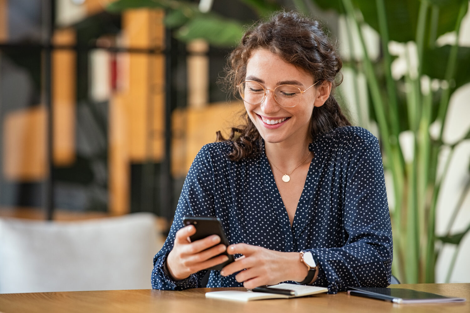 young smiling woman with brown hair and glasses looking at her phone