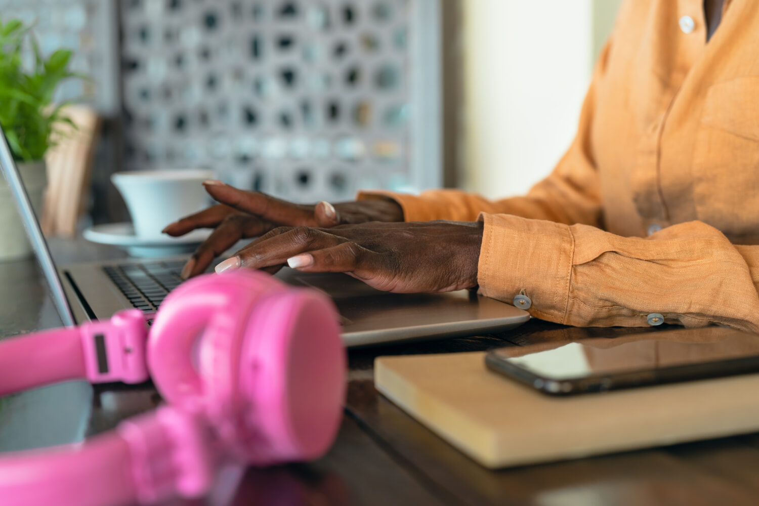 cropped photo of african american woman typing on her computer with pink headphones nearby