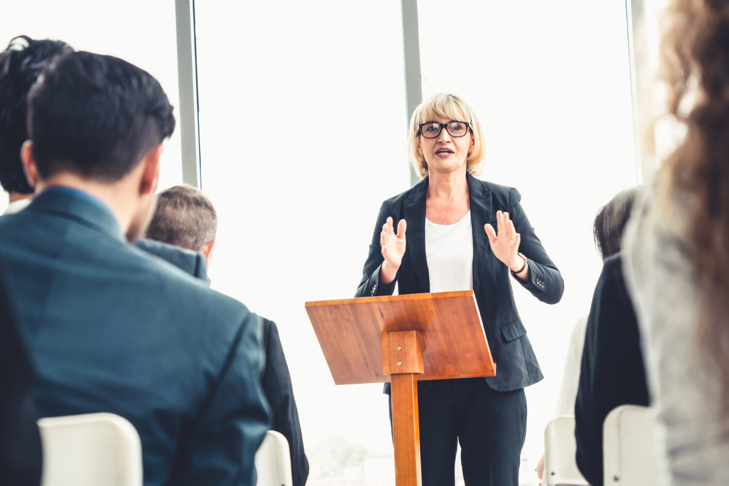 a blonde female stands at a podium and presents to businesspeople