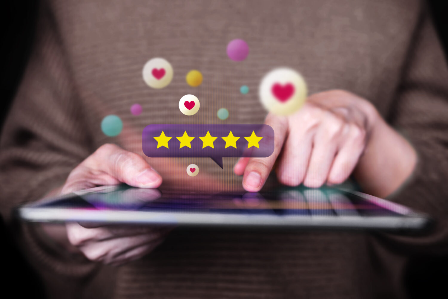cropped image of hands using a tablet with floating star rating and hearts around