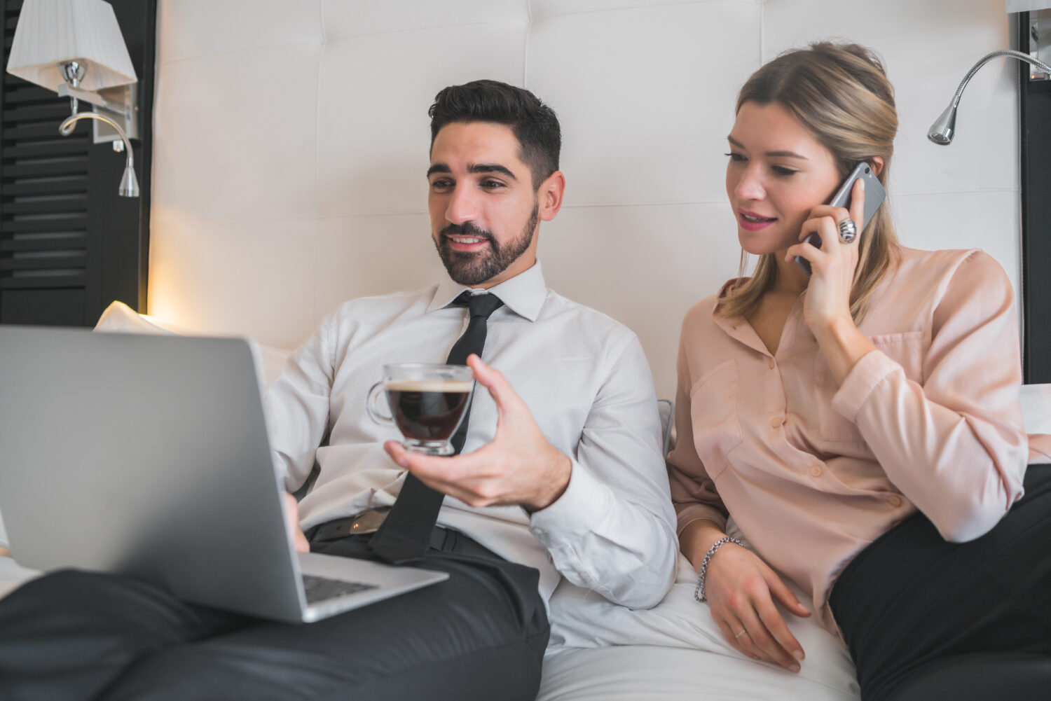 two young business people sitting on a bed and looking at a laptop together