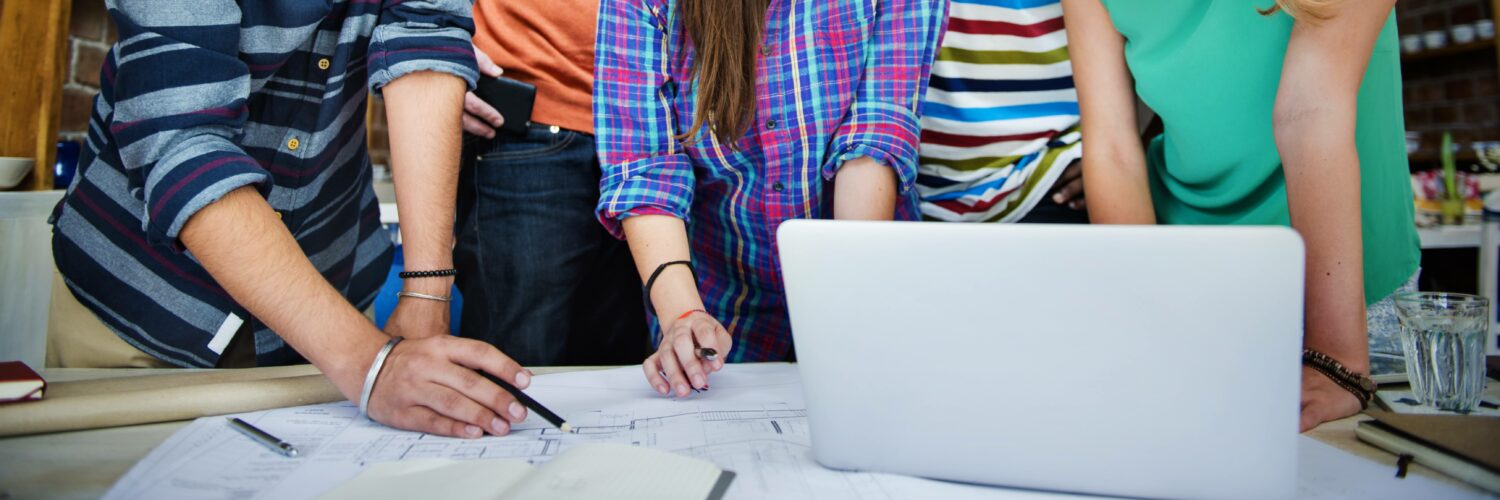 coworkers looking over a blueprint with laptop nearby and writing on the paper