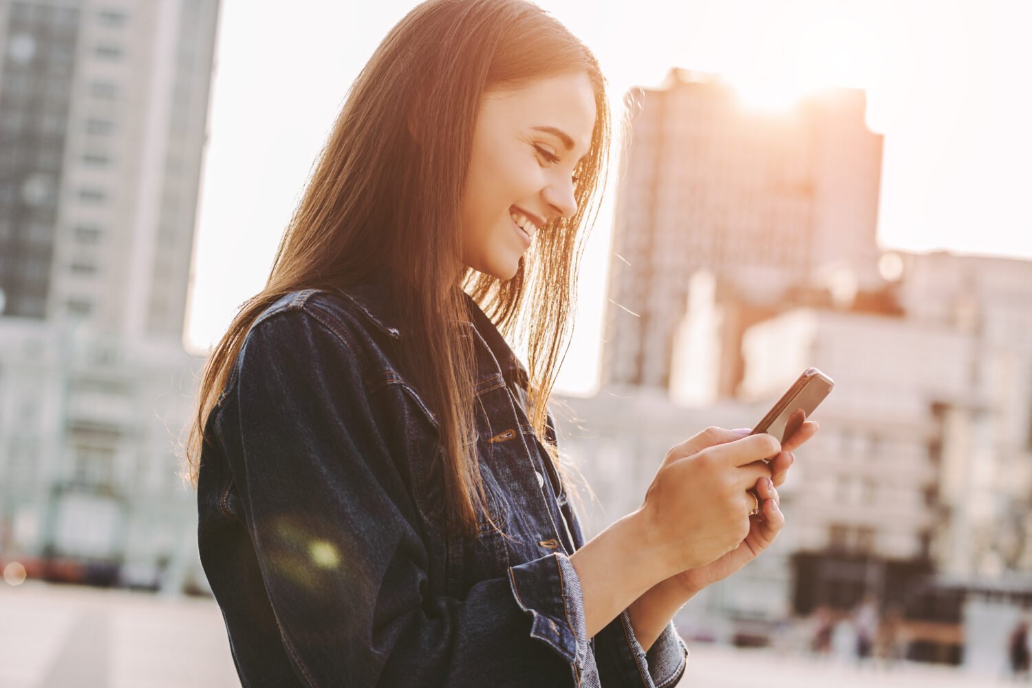 woman walking through city smiling at her phone