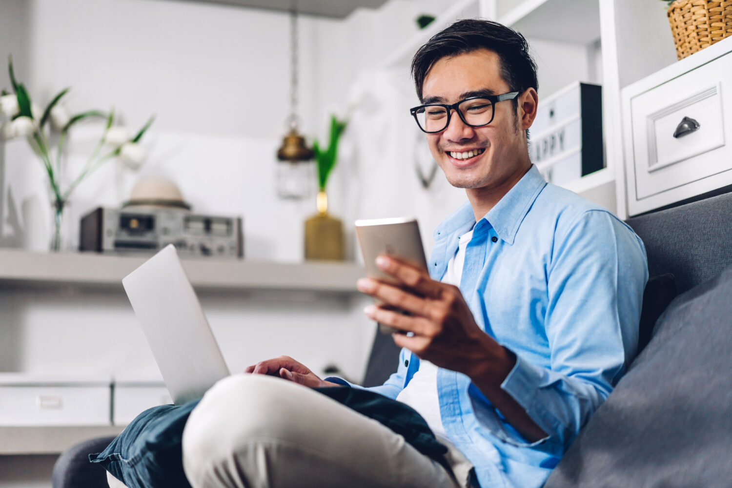 young smiling asian man relaxing using laptop and smiling at phone