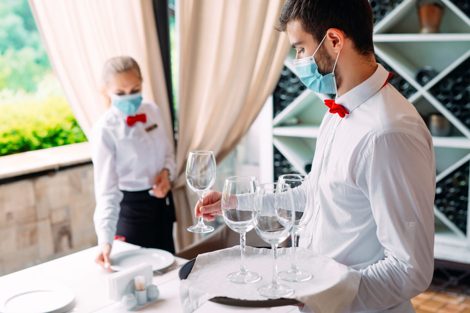 a waiter and his supervisor set a table with wine glasses