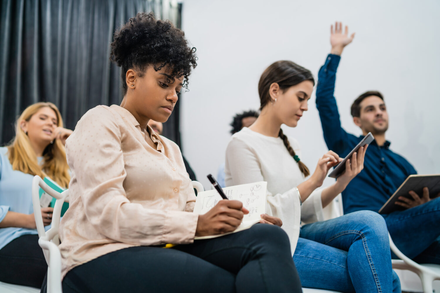 Group of young people sitting on conference together while raising their hands to ask a question