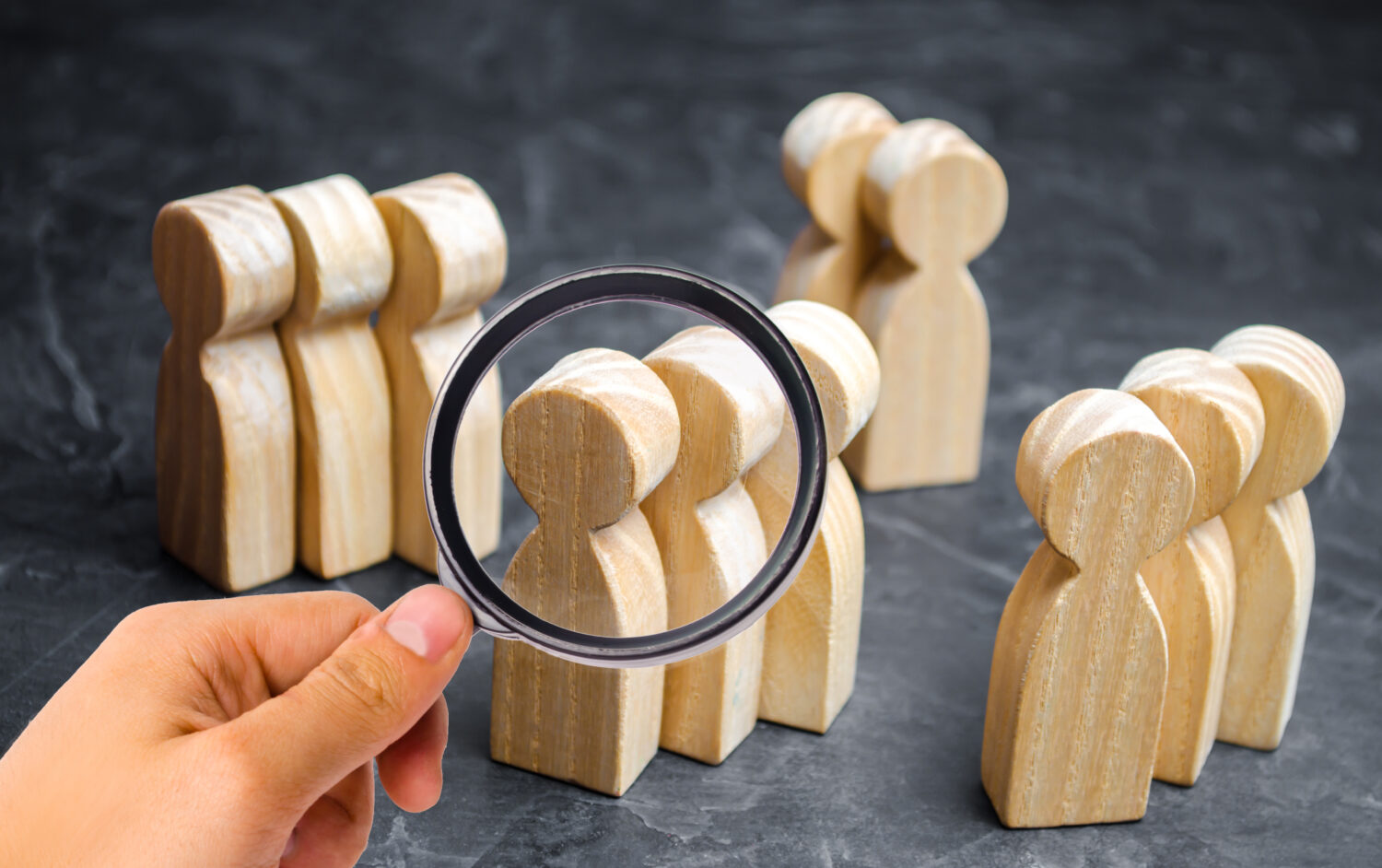 groups of wooden people with a hand holding a magnifying glass to look at them