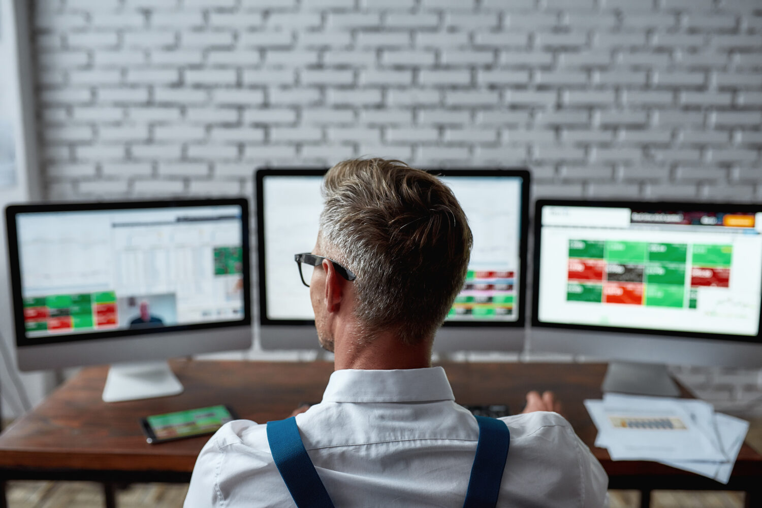 rear view of middle aged man looking at results for surveys on three monitors