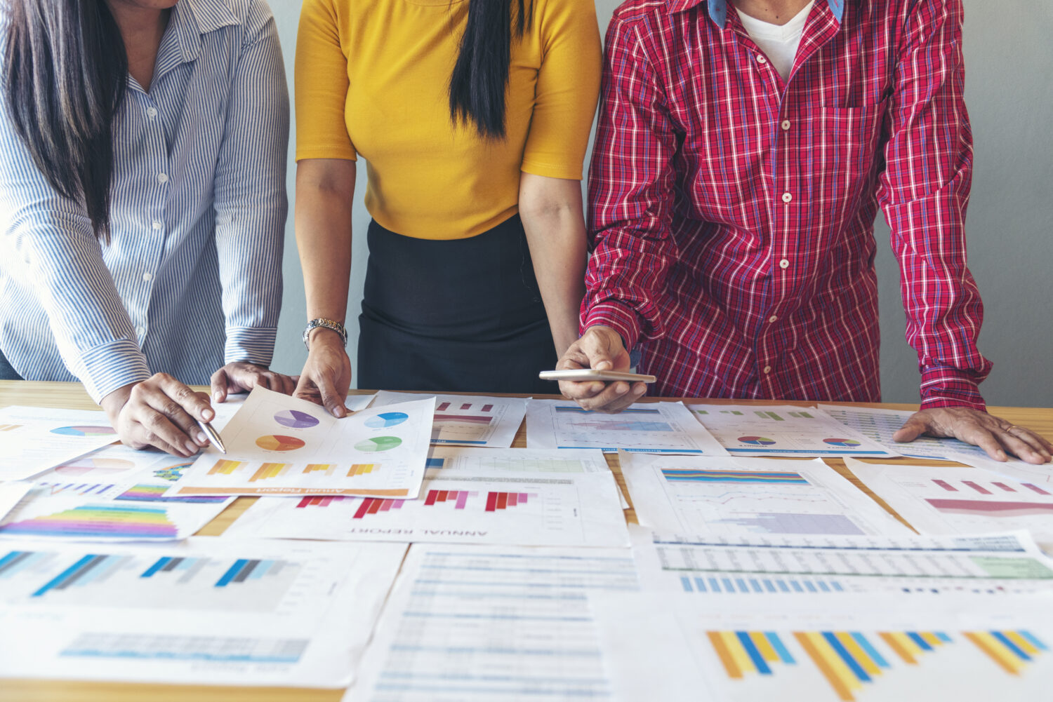 three people standing over a table covered in business charts and graphs