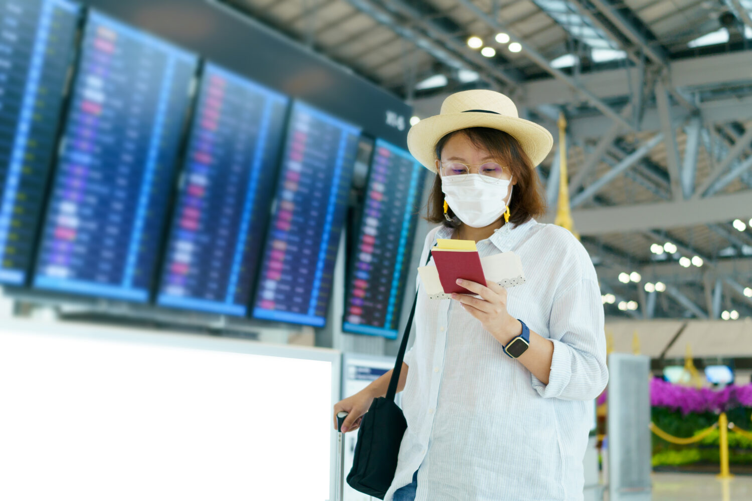 woman in a mask in airport terminal looking down at her phone